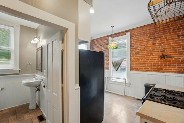 696 Bank St, Columbus, OH 43206 - kitchen featuring a wainscoted wall, stone finish flooring, black gas range oven, decorative light fixtures, and brick wall
