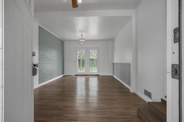 unfurnished room featuring wood finished floors, a chandelier, baseboards, brick wall, and a textured ceiling