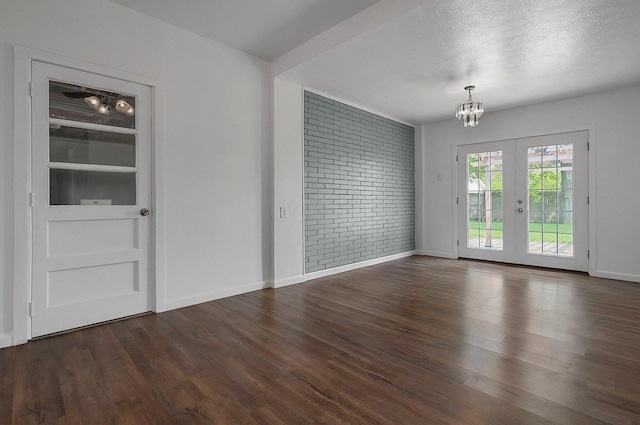 empty room with a chandelier, french doors, wood finished floors, baseboards, and brick wall