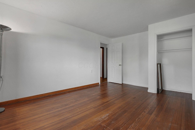 unfurnished bedroom with dark wood finished floors, baseboards, and a closet