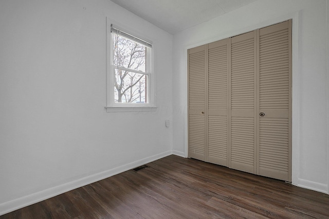 unfurnished bedroom with baseboards, a closet, and dark wood-style flooring