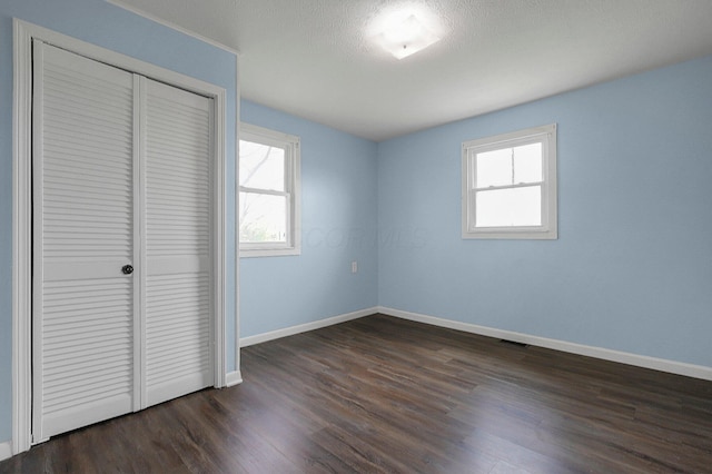 unfurnished bedroom with multiple windows, a closet, dark wood-style floors, and baseboards
