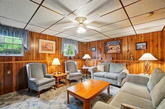 carpeted living area featuring wood walls, ceiling fan, and a drop ceiling