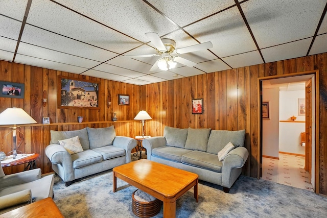 carpeted living room featuring wooden walls, ceiling fan, and a drop ceiling