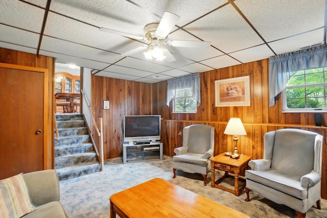living room featuring healthy amount of natural light, wood walls, stairs, a drop ceiling, and carpet floors
