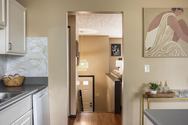 kitchen with dishwasher, tasteful backsplash, dark countertops, wood finished floors, and white cabinets