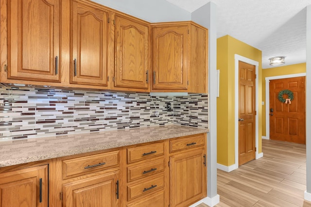 113 Bridgeport Way, Delaware, OH 43015 - kitchen featuring decorative backsplash, light wood finished floors, light stone counters, a textured ceiling, and brown cabinetry
