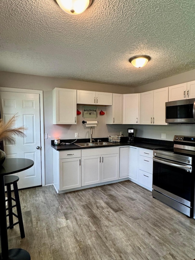 965 Bikini Dr, Marion, OH 43302 - kitchen featuring appliances with stainless steel finishes, a textured ceiling, white cabinets, wood finished floors, and dark countertops
