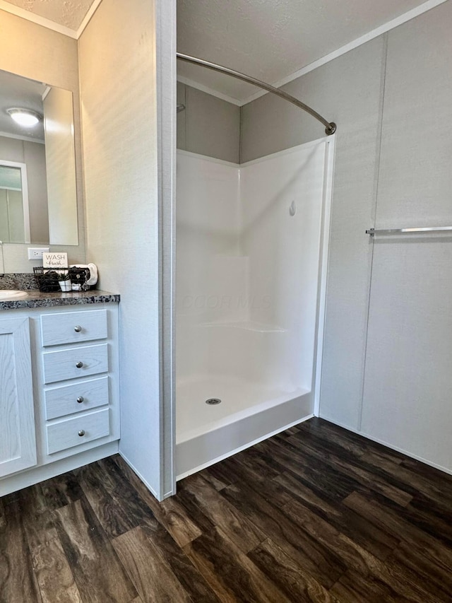 bathroom featuring wood finished floors, walk in shower, ornamental molding, and vanity