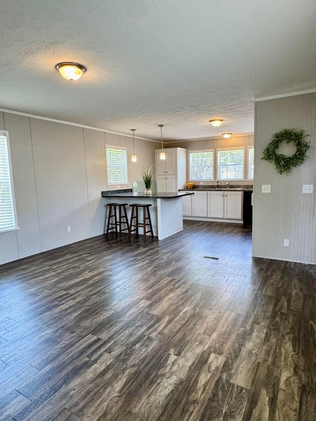 unfurnished living room featuring a textured ceiling, dark wood-style floors, and crown molding