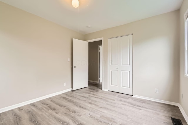 unfurnished bedroom featuring light wood-type flooring, baseboards, and a closet