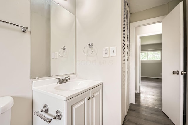 half bathroom with vanity, wood finished floors, and toilet