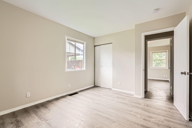 unfurnished bedroom featuring light wood-style floors, baseboards, and a closet