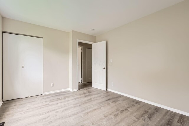 unfurnished bedroom featuring light wood-type flooring, baseboards, and a closet