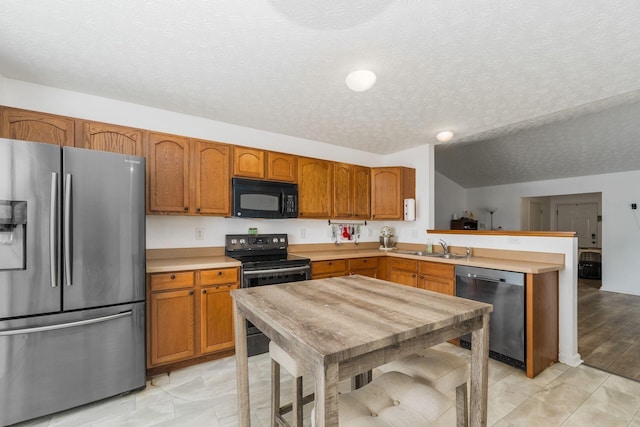 kitchen featuring stainless steel appliances, a textured ceiling, a peninsula, light countertops, and brown cabinetry