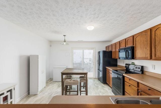kitchen with black appliances, light wood-style floors, brown cabinets, pendant lighting, and a textured ceiling
