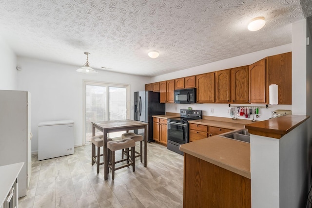 kitchen with appliances with stainless steel finishes, brown cabinets, decorative light fixtures, and a textured ceiling