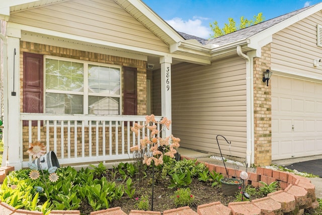 entrance to property with covered porch, an attached garage, and roof with shingles