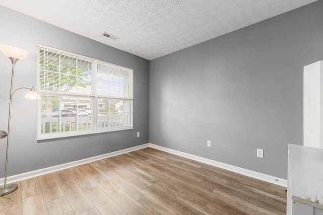 spare room featuring wood finished floors, a textured ceiling, and baseboards