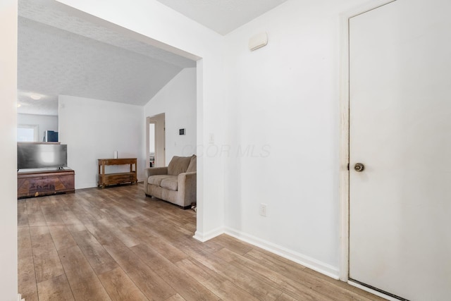 unfurnished room with lofted ceiling, light wood finished floors, a textured ceiling, and baseboards