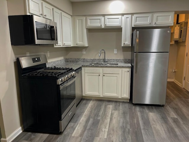 kitchen with appliances with stainless steel finishes, a sink, wood finished floors, light stone counters, and baseboards