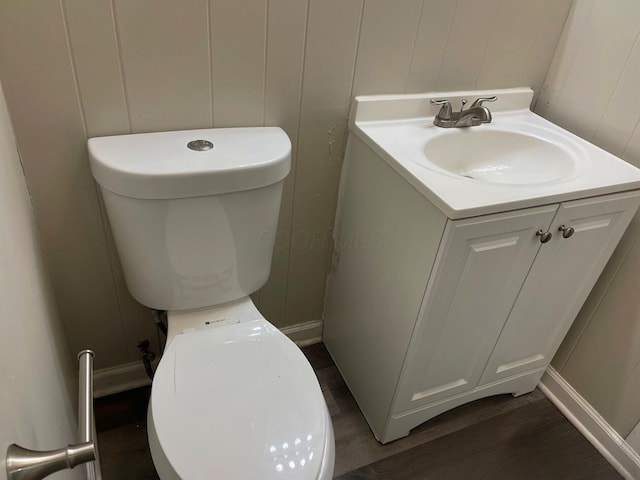 bathroom with a decorative wall, wood finished floors, vanity, toilet, and baseboards