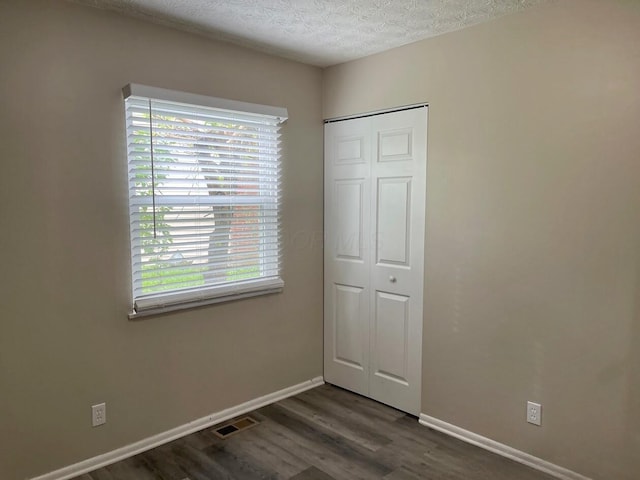 unfurnished bedroom with multiple windows, dark wood finished floors, baseboards, a closet, and a textured ceiling