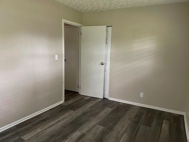 spare room featuring dark wood-type flooring, baseboards, and a textured ceiling