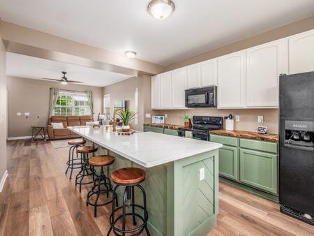 592 Summer Tree Loop, Marysville, OH 43040 - kitchen with black appliances, green cabinets, open floor plan, a kitchen breakfast bar, and light wood-type flooring