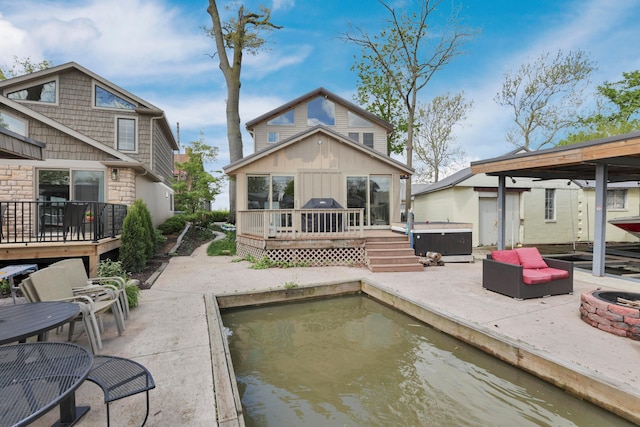 back of property with a hot tub, a deck, a patio area, board and batten siding, and stone siding