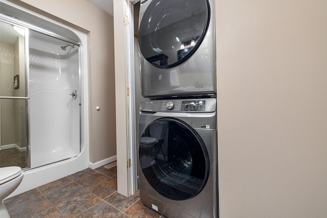 washroom with stacked washing machine and dryer, dark stone finish flooring, and baseboards