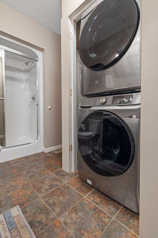 clothes washing area featuring stacked washer / drying machine, dark stone finish floors, and baseboards