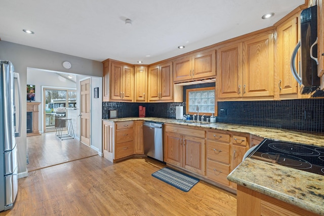 kitchen featuring stainless steel appliances, a sink, light stone counters, light wood finished floors, and tasteful backsplash