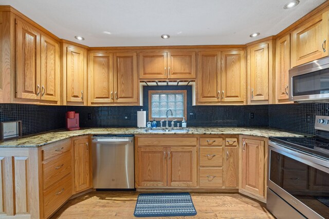 kitchen with stainless steel appliances, a sink, decorative backsplash, recessed lighting, and light stone countertops
