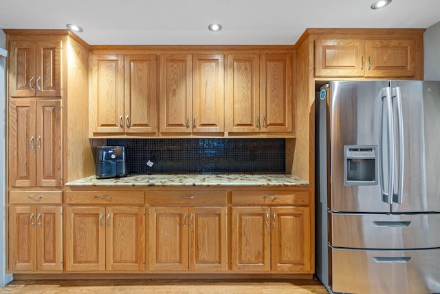 kitchen with stainless steel fridge, light stone counters, backsplash, recessed lighting, and brown cabinetry