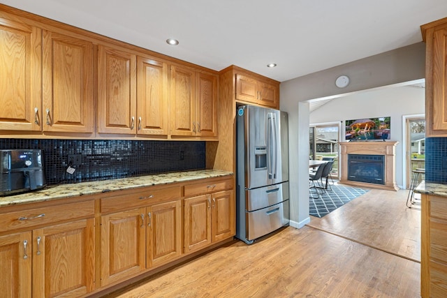 kitchen with stainless steel fridge with ice dispenser, decorative backsplash, light wood finished floors, light stone counters, and brown cabinetry