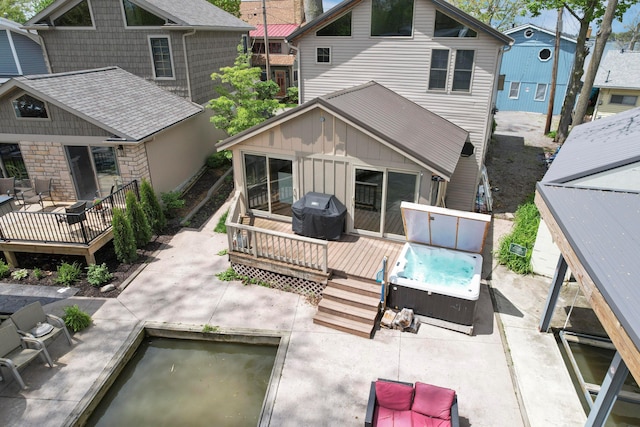 rear view of house featuring a hot tub, a wooden deck, a patio area, and board and batten siding