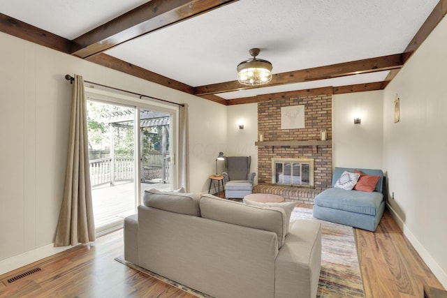 living room with beam ceiling, wood finished floors, a fireplace, and baseboards