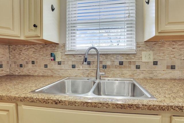 kitchen featuring a sink, light countertops, cream cabinetry, and decorative backsplash