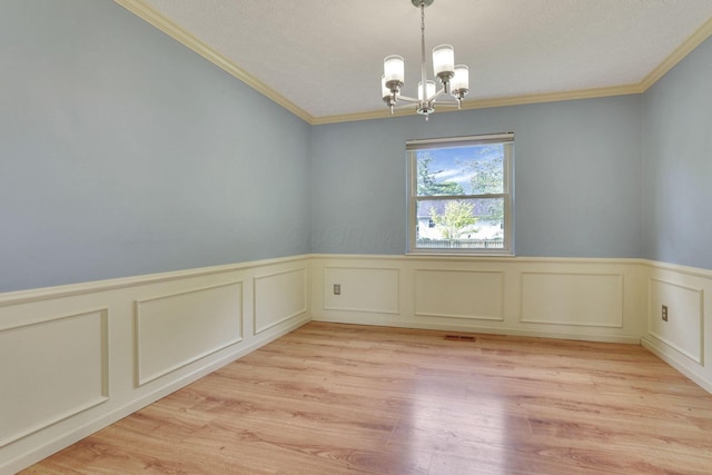 spare room with a chandelier, crown molding, wainscoting, a decorative wall, and light wood-type flooring
