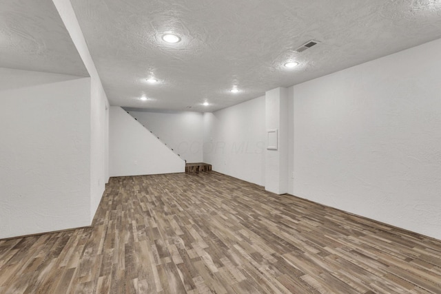 finished below grade area featuring wood finished floors, a textured ceiling, recessed lighting, and a textured wall