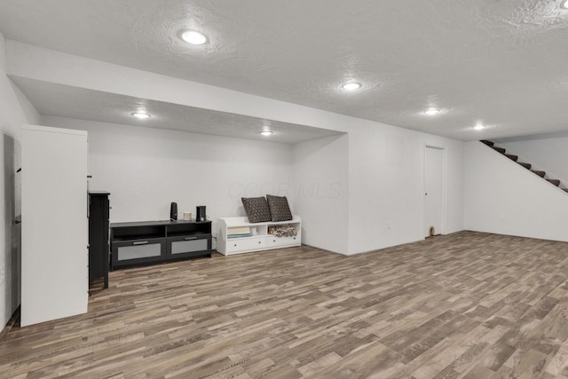 finished basement with wood finished floors, a textured ceiling, stairs, and recessed lighting