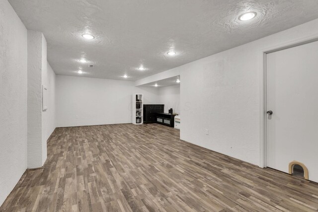 finished below grade area with wood finished floors, recessed lighting, a textured wall, and a textured ceiling