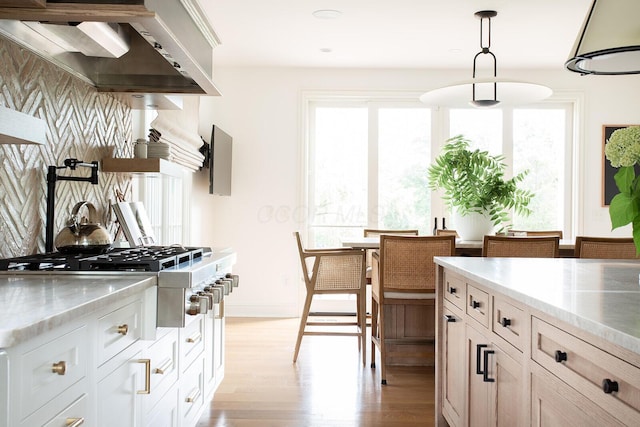 8070 Harriott Rd, Dublin, OH 43017 - kitchen featuring light wood-style flooring, stainless steel gas stovetop, wall chimney exhaust hood, and healthy amount of natural light