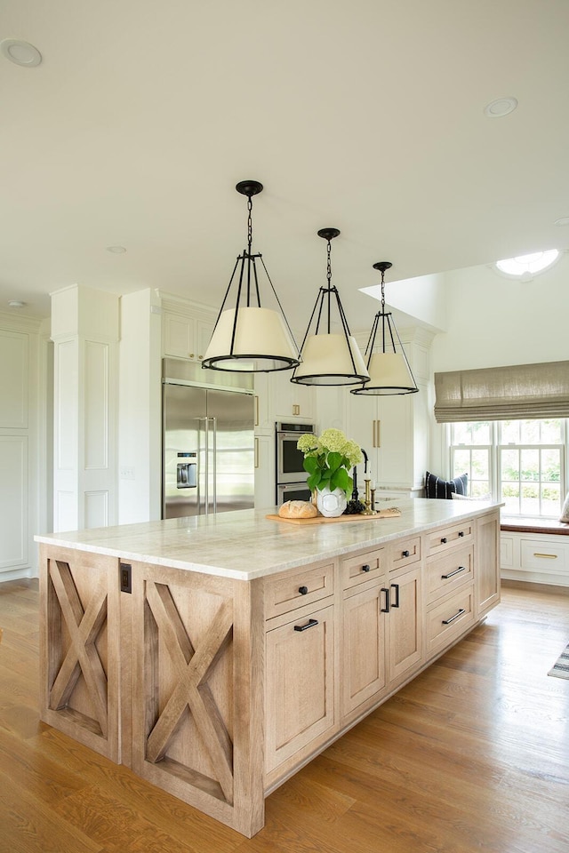 8070 Harriott Rd, Dublin, OH 43017 - kitchen featuring appliances with stainless steel finishes, a spacious island, light wood finished floors, light stone counters, and pendant lighting