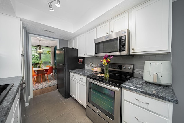 kitchen with stainless steel appliances, white cabinetry, tasteful backsplash, tile patterned floors, and dark stone countertops