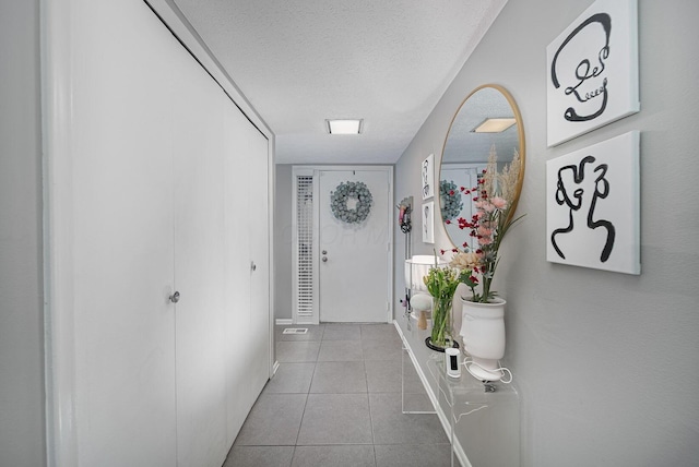 doorway with a textured ceiling, tile patterned floors, and baseboards
