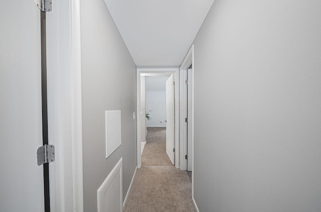 hallway featuring light colored carpet and baseboards