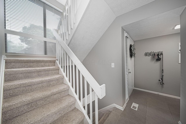 stairway with a textured ceiling, tile patterned flooring, and baseboards
