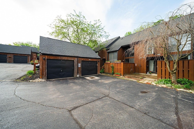 view of front facade with roof with shingles, an outbuilding, fence, and a garage